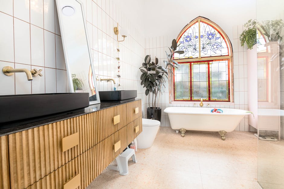 A bathroom with a large, free-standing clawfoot bathtub positioned in front of an arched window with stained glass floral designs, allowing natural light to illuminate the space. To the left, a modern